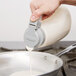 A person using a Tablecraft 48 oz. Dispenser Jar to pour milk into a pan.
