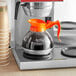 An Avantco decaf coffee decanter with an orange handle on a counter.