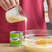 A person pouring California Farms Organic Sweetened Condensed Milk into a bowl of food.