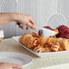 A hand using a Choice stainless steel pastry tong to serve a croissant onto a white plate.