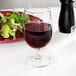 A Libbey Vina wine goblet filled with red wine next to a plate of salad.