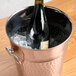 A bottle of wine in a hammered copper wine bucket on a table.