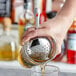 A hand using a Choice stainless steel Julep strainer to pour liquid into a glass on a counter.
