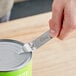 A hand uses a Choice 4" Church Key Can and Bottle Opener to open a can on a table in a home kitchen.