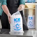 A person in a black apron holding a Choice clear plastic drawstring ice bag filled with ice cubes.