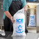 A man in a black apron using a Choice clear plastic drawstring ice bag to fill a bag of ice.