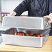 A person holding a Vollrath aluminum roasting pan with food inside.