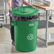 A woman putting a black garbage bag into a green Lavex recycling can.