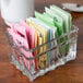 A clear glass Libbey sugar package holder filled with different colored packets.