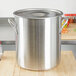A large silver Vollrath stainless steel stock pot with a lid on a wooden surface.