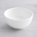 An Acopa Cordelia bright white bowl with an embossed rim on a gray marble surface.