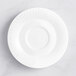 An Acopa Cordelia bright white porcelain saucer with an embossed rim on a white surface.