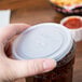 A hand holding a translucent plastic lid with a straw slot over a drink.