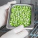 A person in white gloves holding a stainless steel steam table pan of peas.