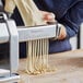 A woman using an Imperia Fettucine Pasta Cutter to make noodles on a counter.