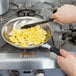 A hand using a Vollrath stainless steel frying pan to cook scrambled eggs.
