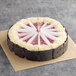 A white chocolate raspberry cheesecake with white frosting and red raspberry swirls.