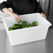 A chef in a black shirt putting green peppers in a white Rubbermaid food storage container.