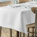 A rectangular white table cover on a table with plates and glasses.