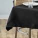 A table with a black Choice square table cover with a white plate and a glass on it.