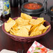 A Raspberry polyethylene round weave basket filled with tortilla chips and a bowl of salsa on a table.