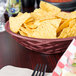 A round polyethylene basket filled with tortilla chips on a table.