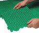 A person's hands interlocking green vinyl Cactus Mat floor tiles.