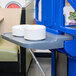 A Cambro navy blue end table with a stack of white plates on it.