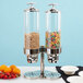 A Vollrath Somerville double canister cereal dispenser with colorful cereal and oranges on a table.