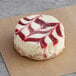 A round white cheesecake with red swirls on top.