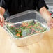 A person holding a plastic container with a salad inside.