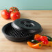 A black round polyethylene tortilla server with a lid on a table with tomatoes.