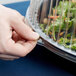 A person putting a salad in a plastic container with a clear plastic high dome lid.