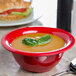 A red Carlisle Sierrus melamine nappie bowl filled with soup with a spoon next to it.