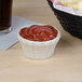 A Hall China ivory flared ramekin filled with ketchup on a table with french fries.