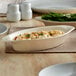 An Acopa ivory oval stoneware rarebit dish with food in it on a table.