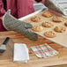 A person in Choice flame retardant oven mitts holding a tray of cookies next to a stack of waffle-weave towels.
