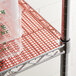 Red plastic mesh shelf liner on a metal shelf with a plastic container.