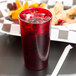 A Cambro ruby red plastic tumbler with a straw in a glass of red liquid on a counter.