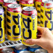 A hand holding a yellow and black C4 Energy Midnight Cherry energy drink can.