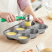 A person using a tool to put yellow liquid into a Choice jumbo muffin tin.