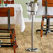 An Acopa stainless steel wine bucket stand with a wine bottle in it on a table.
