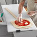 A person using a Choice wooden pizza peel to transfer a pizza to a cutting board on a counter.