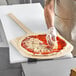 A man using a Choice wooden pizza peel to prepare a pizza.
