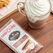 A glass cup of Land O Lakes hot chocolate with whipped cream on top and a packet of Land O Lakes S'mores and Chocolate Cocoa mix.