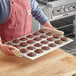 A person holding a tray of muffins using a Choice aluminum muffin pan.