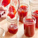 A person pouring red jam into 8 oz. round glass Mason jelly jars.