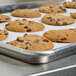A Carlisle wire in rim aluminum sheet pan holding chocolate chip cookies on a metal surface.