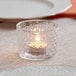 An Acopa hobnail glass votive candle holder with a lit candle inside.