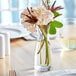 An Acopa glass vase with water and flowers on a table.